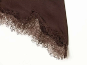 Detail shot of deep brown satin fabric with intricate eyelash lace trim on the garment edge