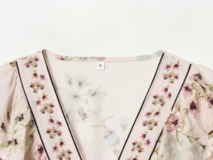 Détail du col en V avec bordure noire et motif floral rose sur une blouse en mousseline