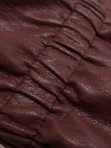 Makroaufnahme einer weinroten Lederjacke mit gesmokter Textur und feiner Ledermaserung