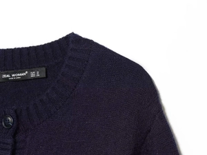 Detailed close-up of dark purple knit cardigan with ribbed neckline and brand label