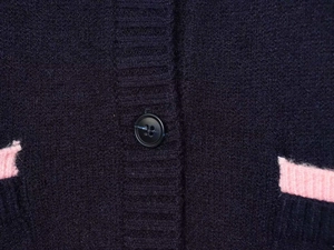 Detail of dark purple knit cardigan with pink trim and matte black button closure
