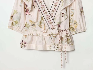 Détail d'un haut cache-cœur floral avec décolleté en V à volants et lien à la taille