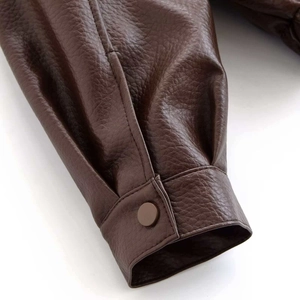 Détail de la manche d'une veste en cuir marron foncé avec texture grainée et bouton pression