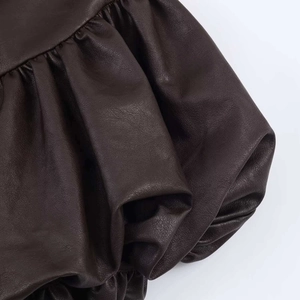 Détail d'une robe en cuir marron foncé avec volants souples et plis texturés sur fond blanc