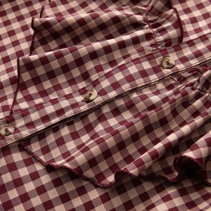 Close-up of red and beige gingham fabric with tiered ruffles and dark wood buttons