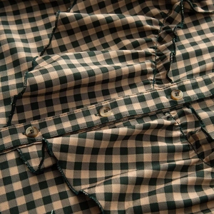 Close-up of green gingham shirt featuring amber buttons and elegant pleated ruffle details