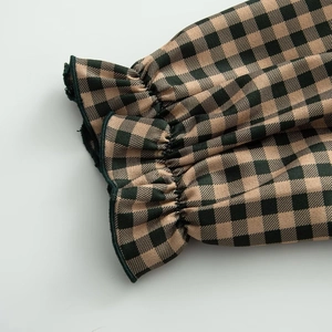 Macro detail of the green gingham shirt showing the elastic shirring and ruffled cuffs