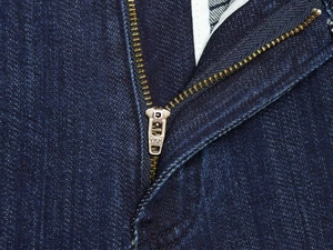 Dettaglio di jeans in denim blu scuro con cerniera in metallo YKK e trama del tessuto pregiato