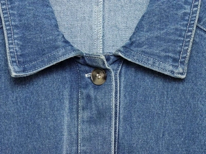 Detailansicht des Denim-Hemdkragens mit Knopf und feiner Nahttextur in Blau