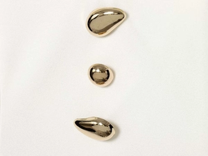 Dettaglio di tre bottoni dorati lucidi con forma a ciottolo geometrico irregolare