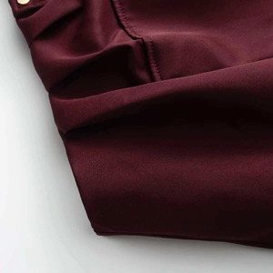 Dettaglio ravvicinato del tessuto twill bordeaux con cuciture precise e rivetti dorati