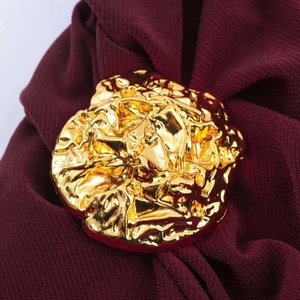 Macro shot of gold liquid metal brooch with textured finish on dark red fabric