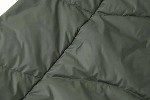 Detailed close-up of dark olive quilted down jacket with waterproof matte fabric and stitching