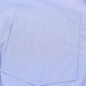 Detailed macro shot of the square chest pocket and stitching on a light blue cotton shirt