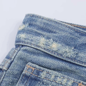 Close-up of light blue wash denim jeans with distressed raw edges and orange stitching