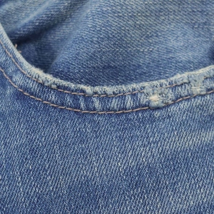Detailed macro view of vintage blue denim fabric with frayed edges and double stitching