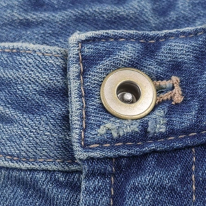 Detailed close-up of bronze metal button and stitching on high-waist blue denim jeans