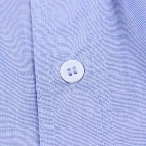 Detailed close-up of a white resin button on a light blue fashion shirt with twill texture