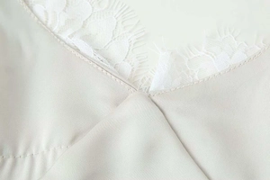 Détail du décolleté en V avec dentelle de cils blanche sur un tissu en satin de champagne