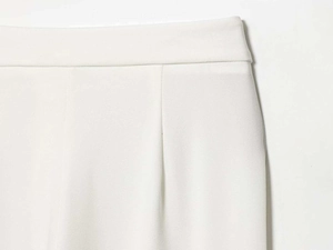 Dettaglio dei pantaloni bianchi a vita alta con eleganti pieghe e trama di tessuto liscio