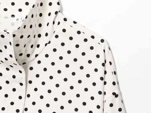 Detail view of white shirt with black polka dots showing size S tag and collar seam