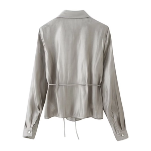 Detail of the back of a silver satin shirt featuring a thin adjustable waist tie and long sleeves
