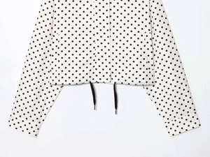 Detailed view of white polka dot jacket featuring black drawstring toggles and front pockets