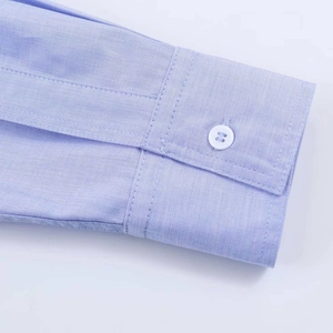 Macro shot of light blue cotton shirt cuff showing neat stitching and white resin button