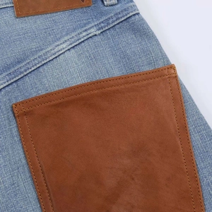 Detail of light blue denim with brown leather pocket patchwork and neat stitching