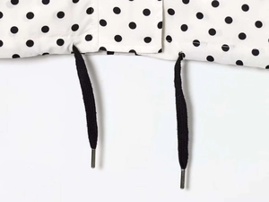 Detail of white polka dot fabric featuring black drawstrings with silver metal tips
