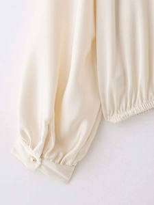 Détail de la manchette en satin blanc cassé avec bouton doré et ourlet plissé