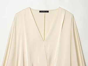 Close-up of elegant champagne satin blouse with V-neck drapes and smooth fabric texture