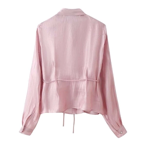 Detail of the back tie design on a pale pink silk-satin shirt with polished fabric texture