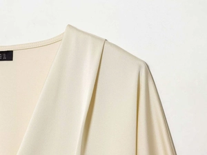 Macro detail of cream satin blouse showing V-neckline, pleats, and global size label