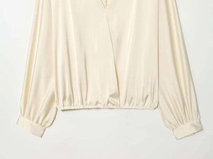 Detail of elegant beige satin shirt featuring V-neckline and smooth silky fabric texture