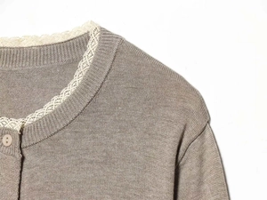 Detail of delicate white lace trim on the collar of a taupe knitted cardigan