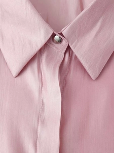 Detailed view of pink satin shirt featuring glossy fabric texture and silver button