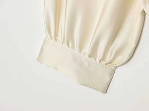 Close-up of elegant pleated cuffs on a smooth champagne satin lantern sleeve blouse