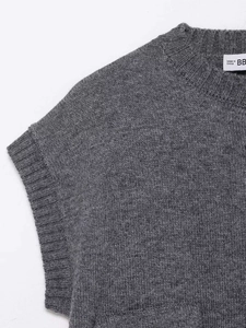 Detail of grey knitted vest neck showing rib trim and brand label on soft fabric