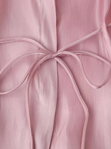 Detailed macro view of smooth pink silk blouse texture with elegant bow tie ribbons