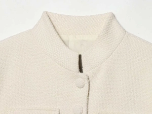 Detailed macro view of cream tweed jacket fabric with textured weave and covered buttons