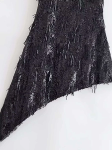 Gros plan du tissu noir à paillettes avec détails de franges et coupe asymétrique
