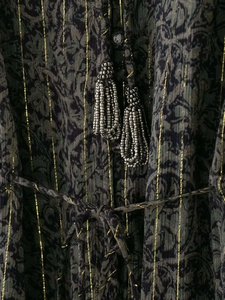 Detail eines Boho-Kleides mit Paisley-Muster, Lurexstreifen und grauen Perlenquasten