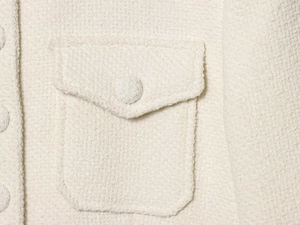 Macro shot of cream tweed fabric texture with a flap pocket and woven button detail