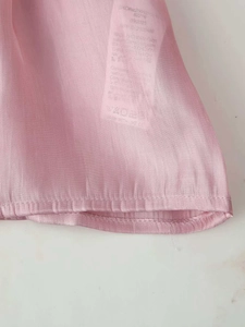 Detail of pink semi-transparent fabric texture with white silk care label and stitching