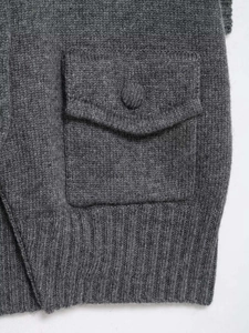 Detail of dark grey knit vest with flap pocket, knit button, and ribbed hem texture