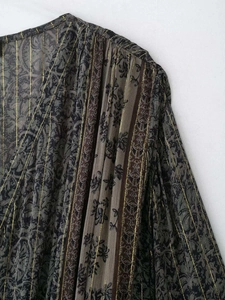 Detailansicht eines Paisley-Kleides mit plissierten goldenen Streifen auf dunklem Stoff