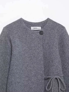 Detailed view of the gray knitted cardigan with round neck and black button closure