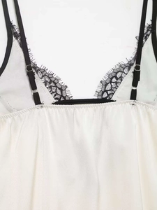 Nahaufnahme eines weißen Satin-Tops mit schwarzem Wimpernspitzenbesatz und Trägern