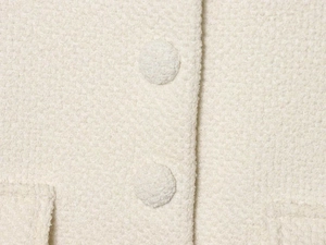 Detail of cream bouclé jacket fabric with textured weave and matching fabric-covered buttons